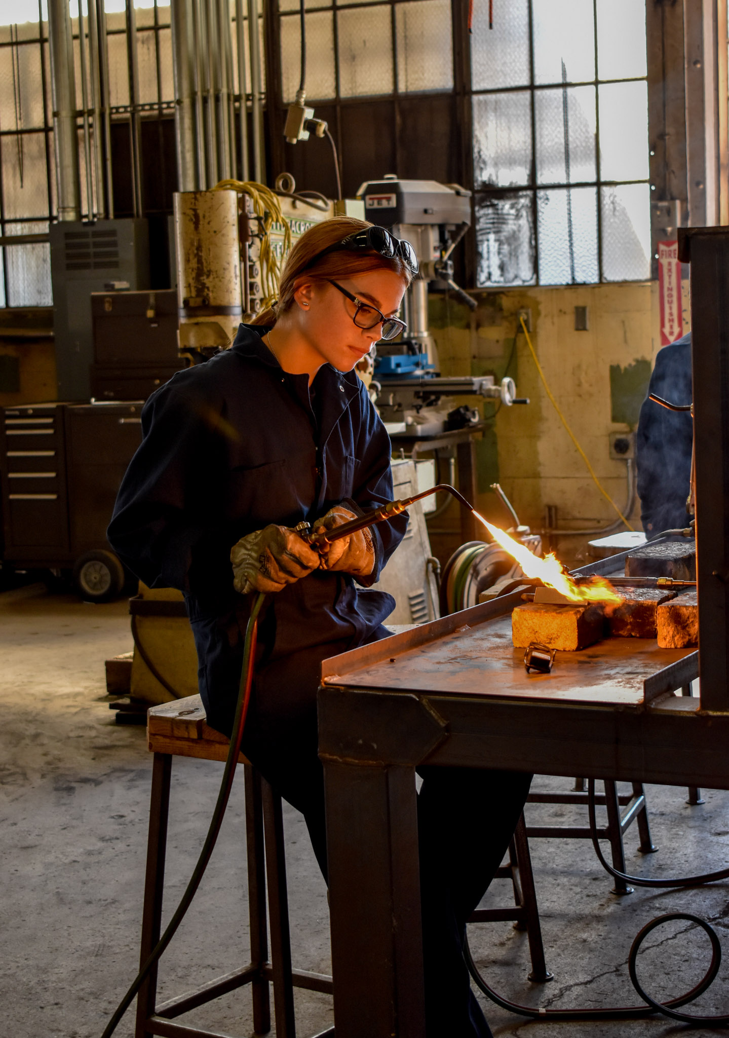 The fire from the blow torch is shining on the girl as she begins the process of welding. This photo was shot with a D3500 camera and a zoom lens.