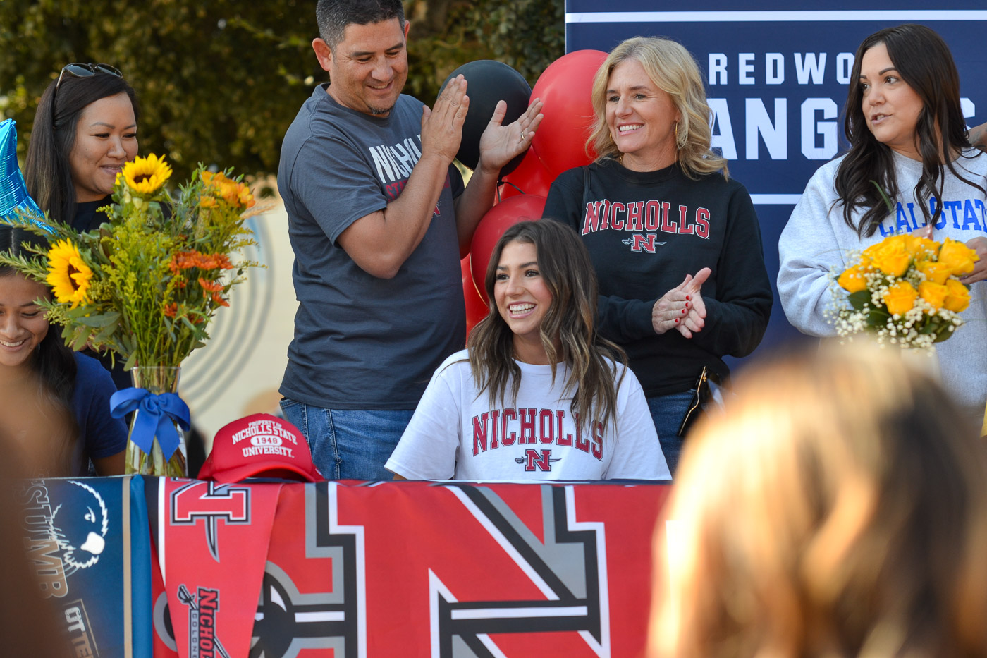 Photos from Signing Day at Redwood High School, taken on November 9, 2023. The images document the event where student athletes announce their commitments to college sports programs. Key moments include athletes signing commitment papers, interacting with coaches and family members, and their reactions during the event. The photographs aim to capture the significance of this day for the students and their supportive community.